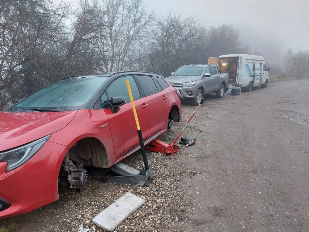 Defektes autó emelőn a ködös út mellett, mögötte a szervizbusz. Helyszíni javítás munka közben.