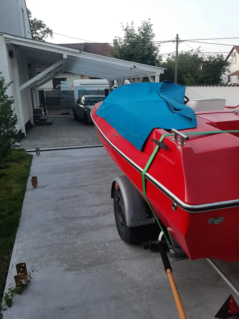 Piros csónak utánfutón egy családi ház udvarán.