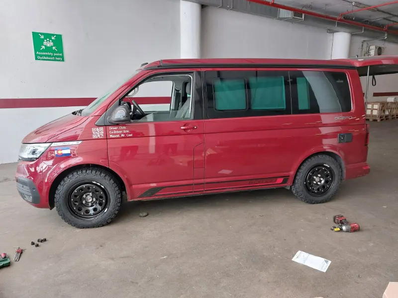 Piros VW California lakóautó kerékcsere közben egy mélygarázsban.